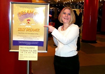 Animated News & Views' Lindsay Mayer stands next to a poster for DREAM ON, SILLY DREAMER.